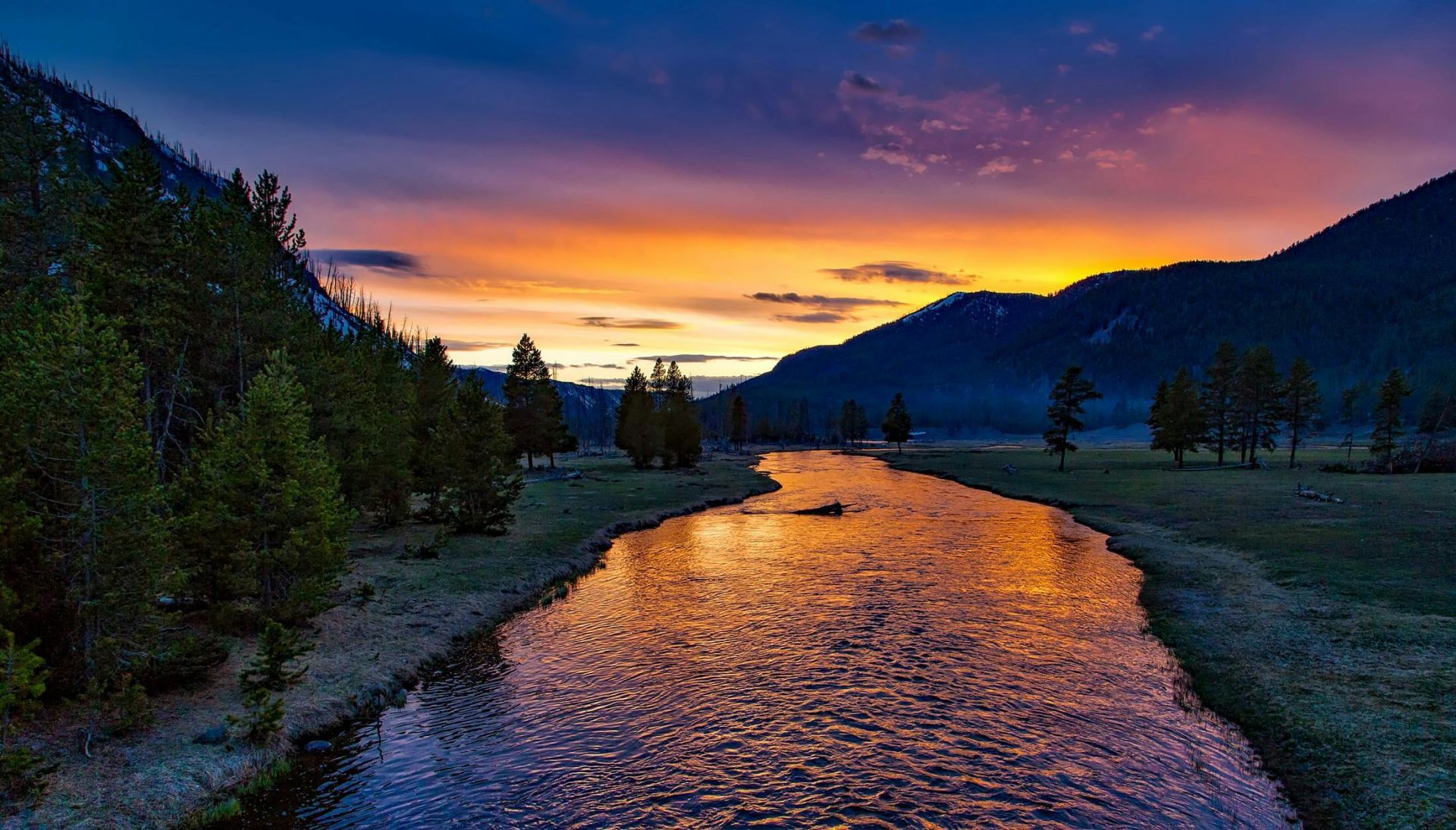 Serene mountain river at sunset with vibrant colors and lush pine trees.