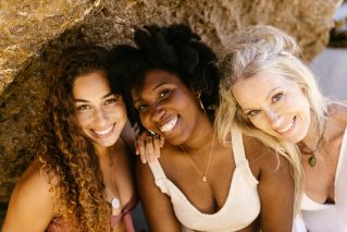 Three diverse women smiling warmly at the camera, celebrating friendship and diversity.