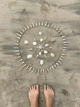Footsteps lead to a creative seashell mandala on a sandy beach, embodying tranquility.